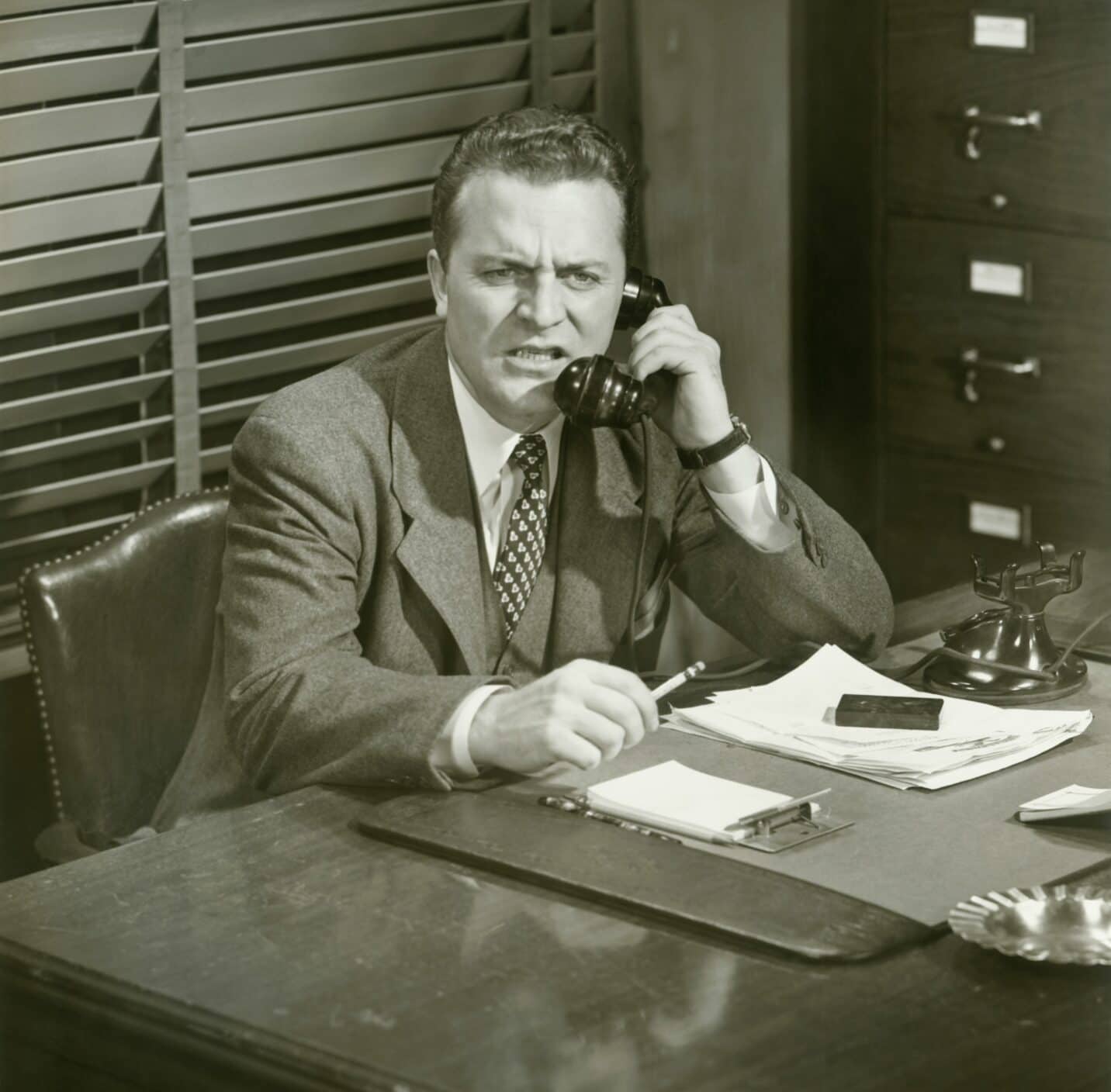 A man sitting at a desk, making a call, with a confused face